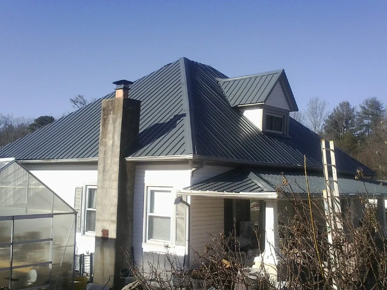 Dark blue standing seam metal roof on a white farmhouse with dormer — Slate & Tile Roof Repair by Roofing Brothers in Strongsville