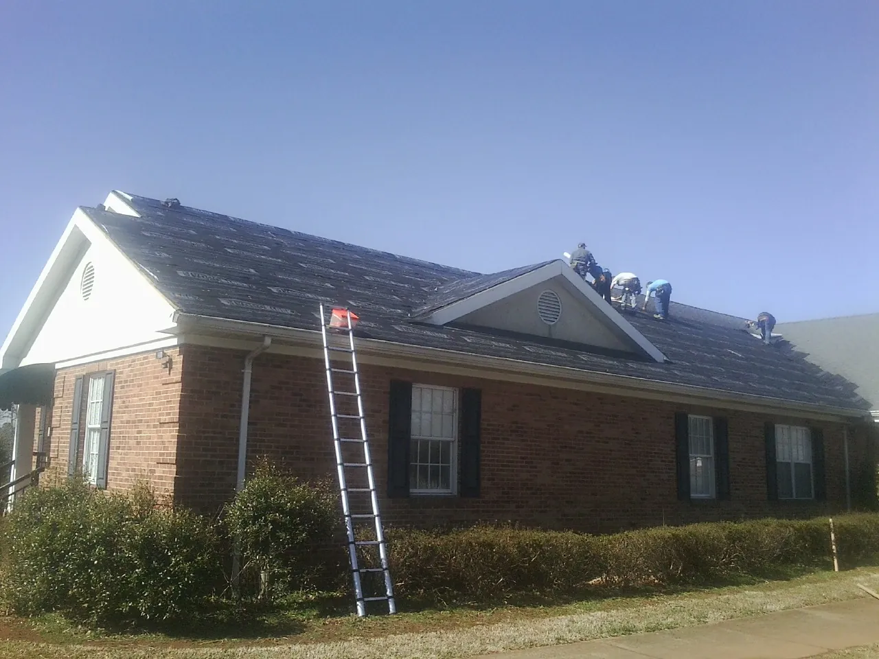 Crew tearing shingles off a brick ranch roof with a ladder set — Emergency Roof Repair work by our crew in Strongsville