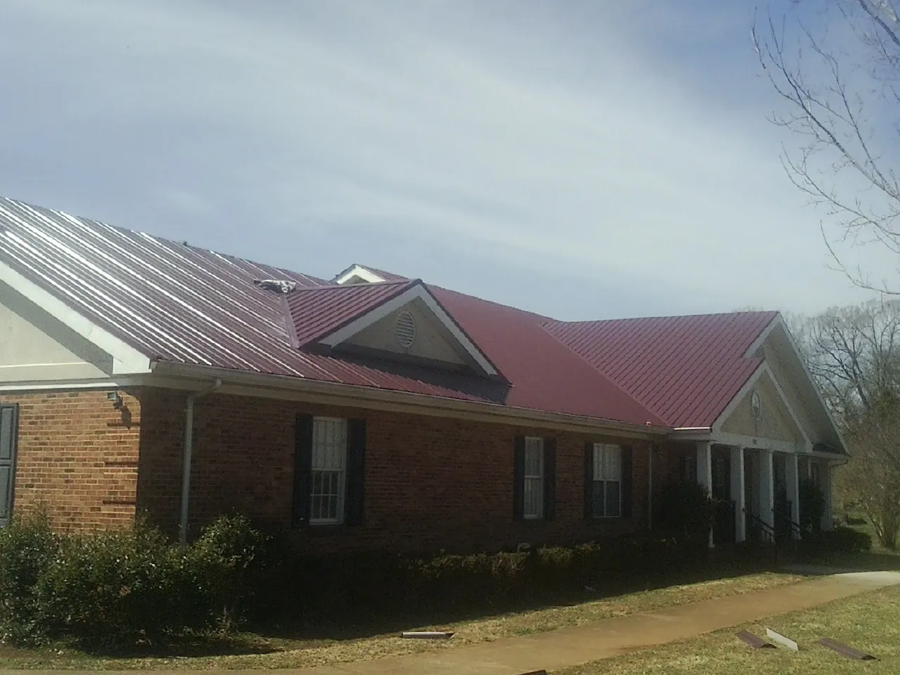 Red metal roof with gabled entries on a long brick building, from a Hail Damage Roof Repair job in Strongsville