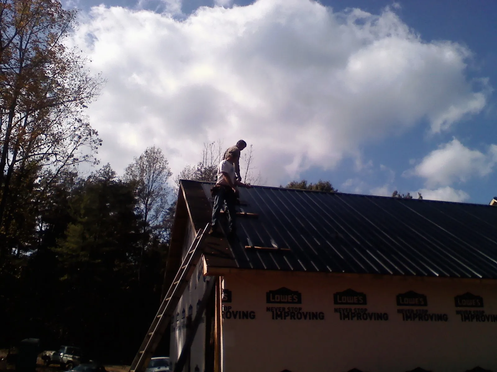Roofer fastening dark metal panels high against a cloudy sky, from a Roof Inspection job in Strongsville