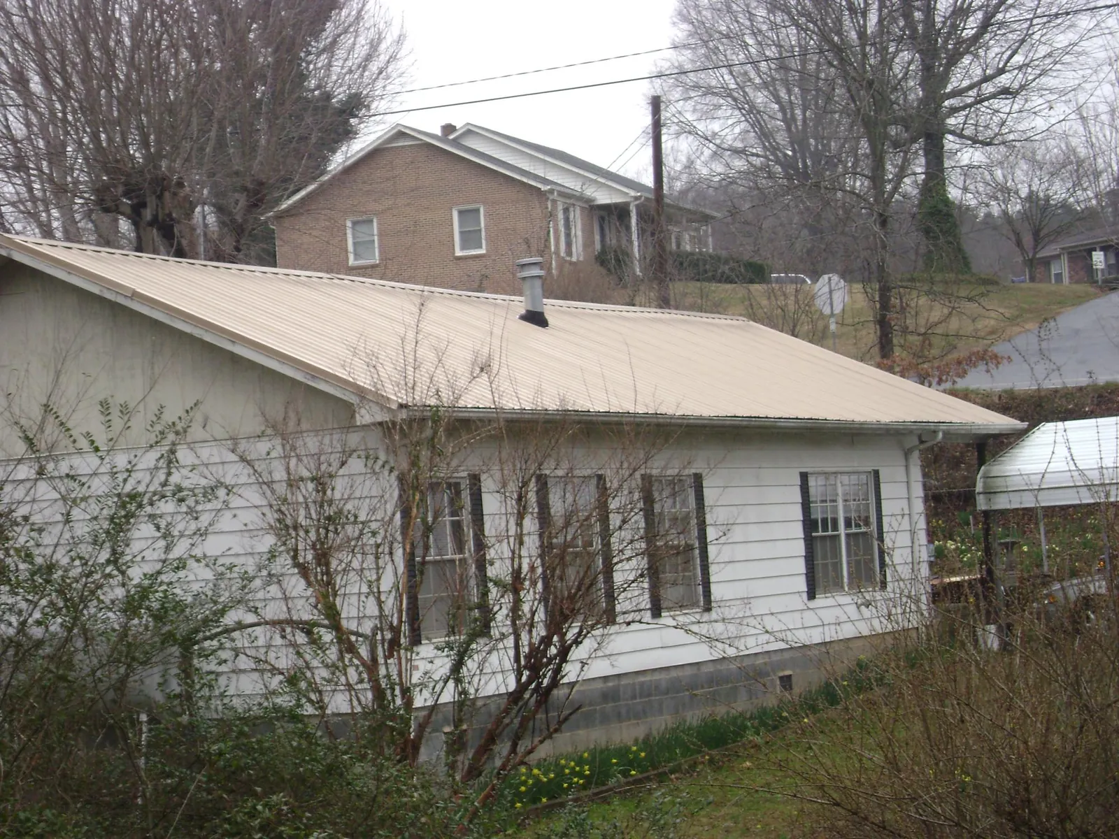 Tan metal roof on a white sided house set into a hillside — Commercial Roofing by Roofing Brothers in Strongsville